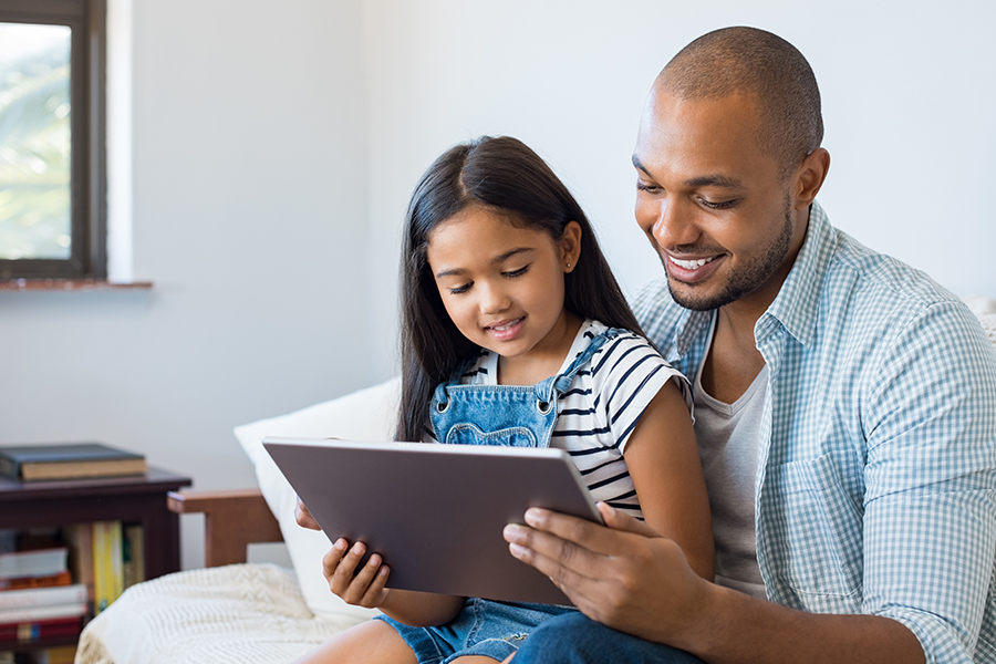 Client Center - Father and Daughter Smiling and Looking at a Tablet Together in Their Living Room